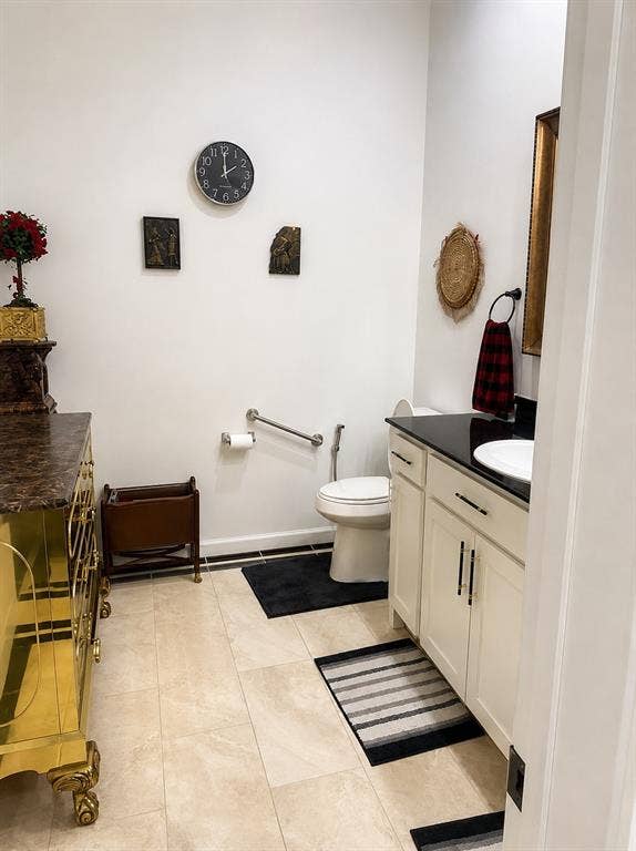 703 E Oates Road, Garland, TX 75043 Light-colored tile flooring, white walls, built-in vanity with white cabinetry, black countertop, and a white basin sink