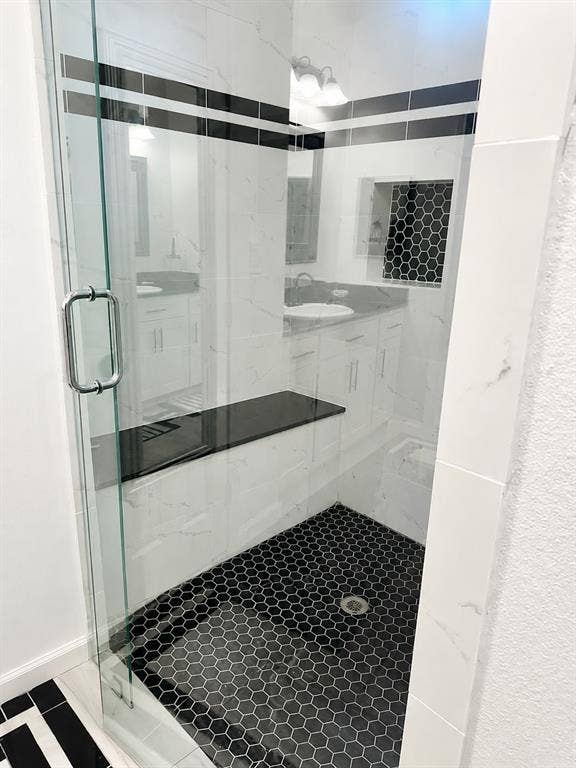 703 E Oates Road, Garland, TX 75043 Glass-enclosed shower with black hexagonal floor tile, white marble-patterned wall tile, a black contrasting accent stripe, a built-in black bench, and a tiled shower niche