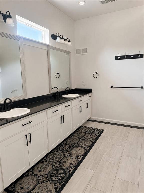 703 E Oates Road, Garland, TX 75043 Dual vanity with dark countertops and white cabinetry, featuring two undermount sinks