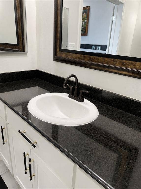 703 E Oates Road, Garland, TX 75043 White vanity with dark stone countertop, undermount sink, and dark bronze faucet