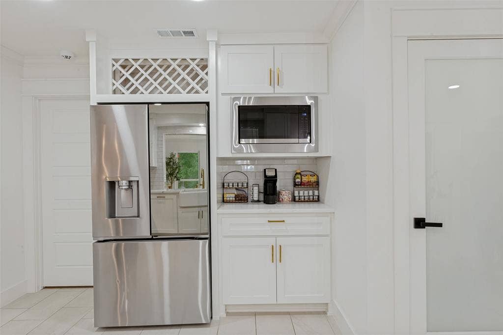 4316 Springbranch Drive, Benbrook, TX 76116 Stainless steel refrigerator, white cabinetry with gold-tone hardware, built-in microwave, white subway tile backsplash, and frosted glass door with black hardware