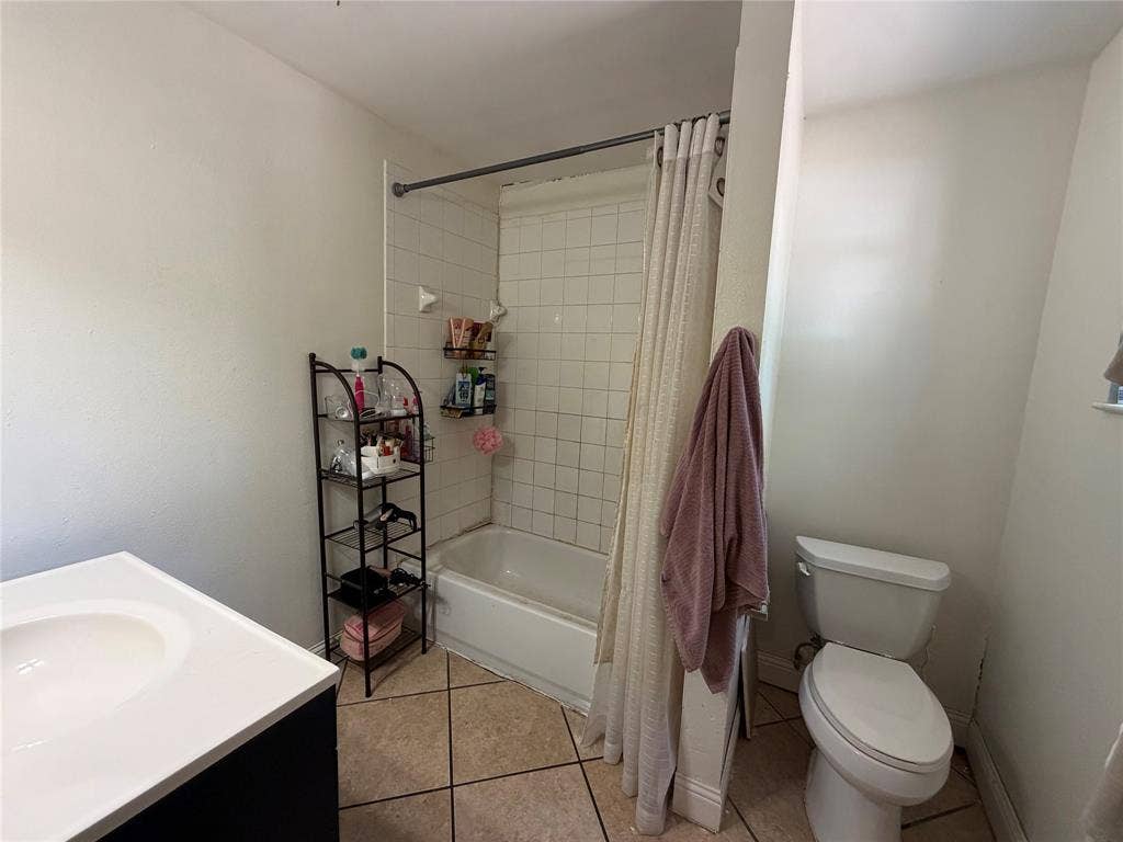 1333 Springlake Drive, Dallas, TX 75217 White ceramic tile shower surround with a built-in tub, white vanity with an integrated sink, and light-toned tile flooring