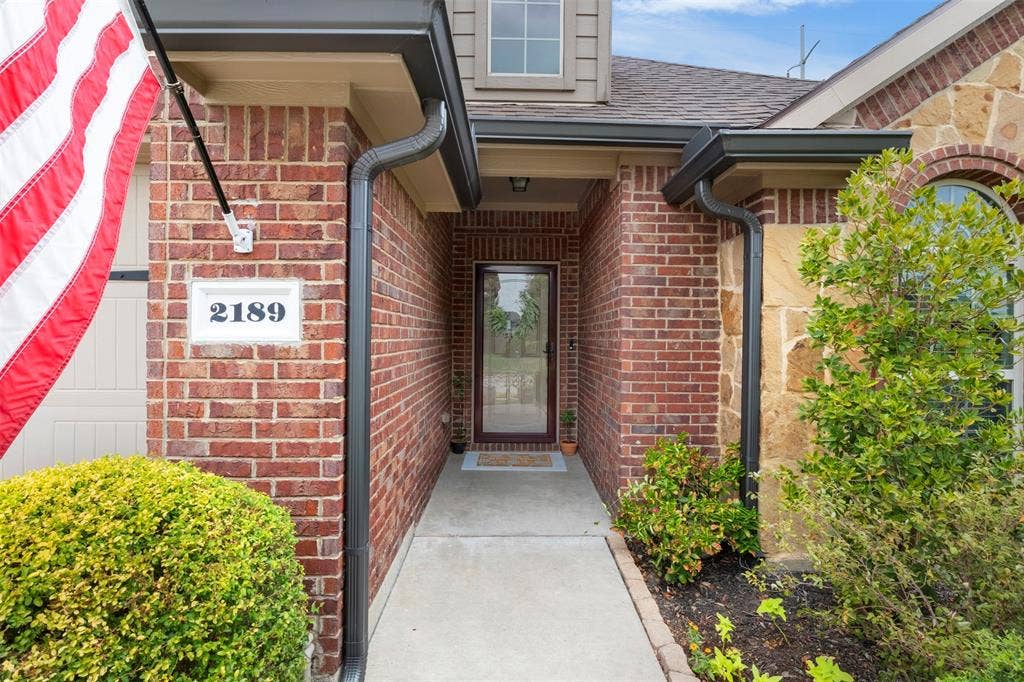 2189 Liriope Lane, Waxahachie, TX 75165 A closer look at the covered front entry, framed by brick and stone details and established landscaping—a welcoming transition into the home's updated interior.