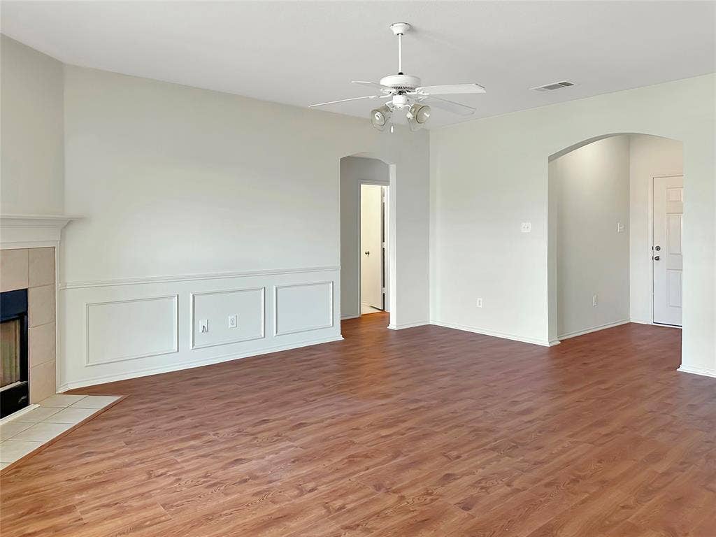 3457 Newgate Street, Midlothian, TX 76065 Unfurnished living room with wood finished floors, arched walkways, a tile fireplace, a ceiling fan, and a decorative wall