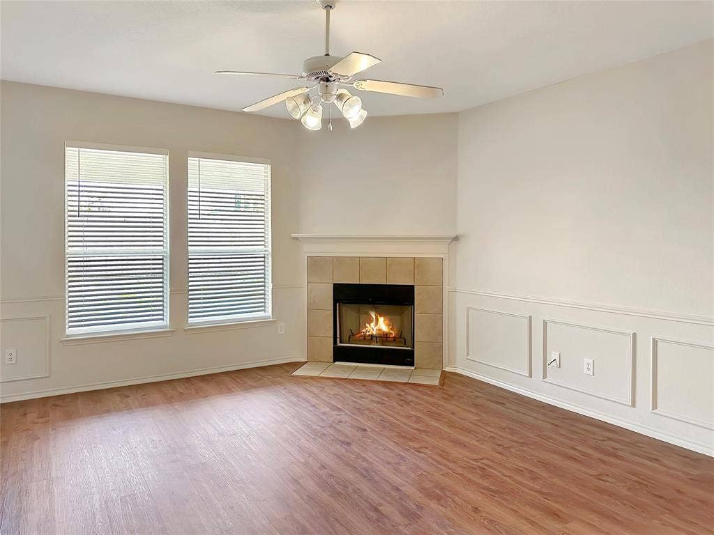3457 Newgate Street, Midlothian, TX 76065 Unfurnished living room with a decorative wall, a tiled fireplace, wainscoting, a ceiling fan, and light wood finished floors