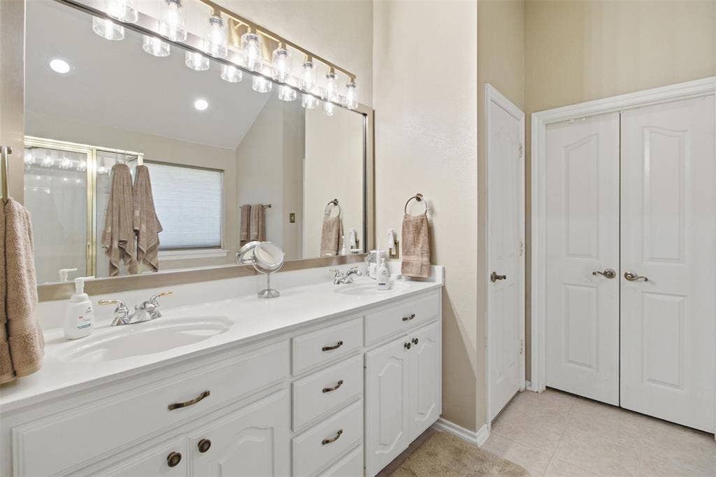 1112 Badbury Lane, Grand Prairie, TX 75052 Dual vanity with white cabinetry, integrated sinks, chrome faucets, and an expansive mirror