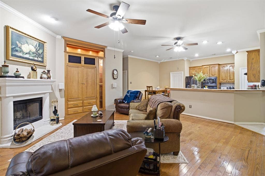 1112 Badbury Lane, Grand Prairie, TX 75052 Hardwood flooring, crown molding, a built-in entertainment center, a fireplace with a mantel, and an open-concept kitchen with wood-finish cabinetry