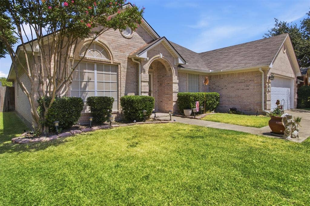 1112 Badbury Lane, Grand Prairie, TX 75052 Brick exterior with an arched entry, prominent front-facing window with an arched transom, and a two-car garage