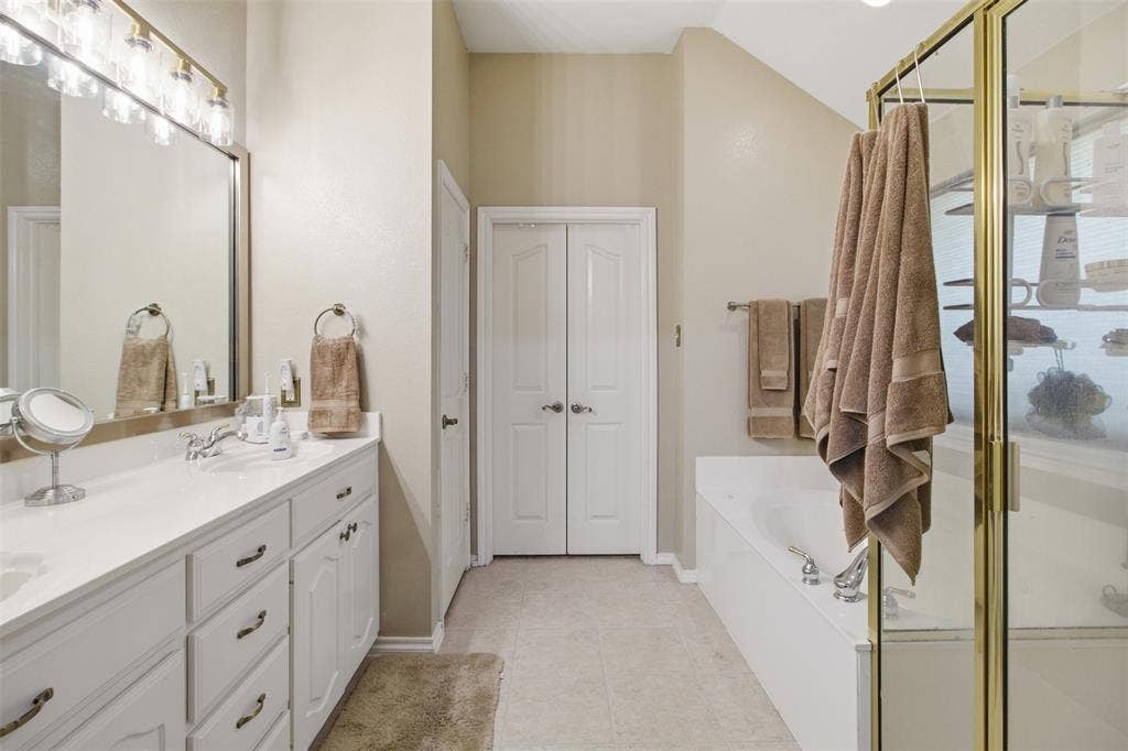 1112 Badbury Lane, Grand Prairie, TX 75052 Dual vanity with white cabinetry and chrome hardware, an integrated soaking tub, a separate glass-enclosed shower, and tile flooring