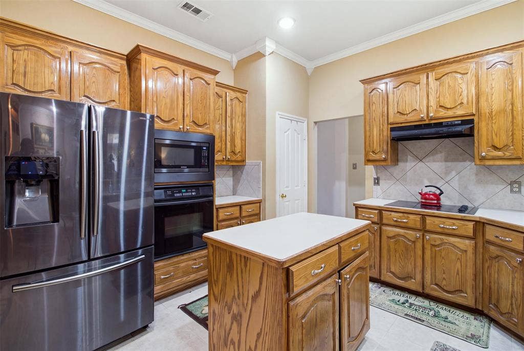 1112 Badbury Lane, Grand Prairie, TX 75052 Kitchen featuring wood cabinetry, stainless steel appliances, a center island with countertop, tile flooring, and a tile backsplash