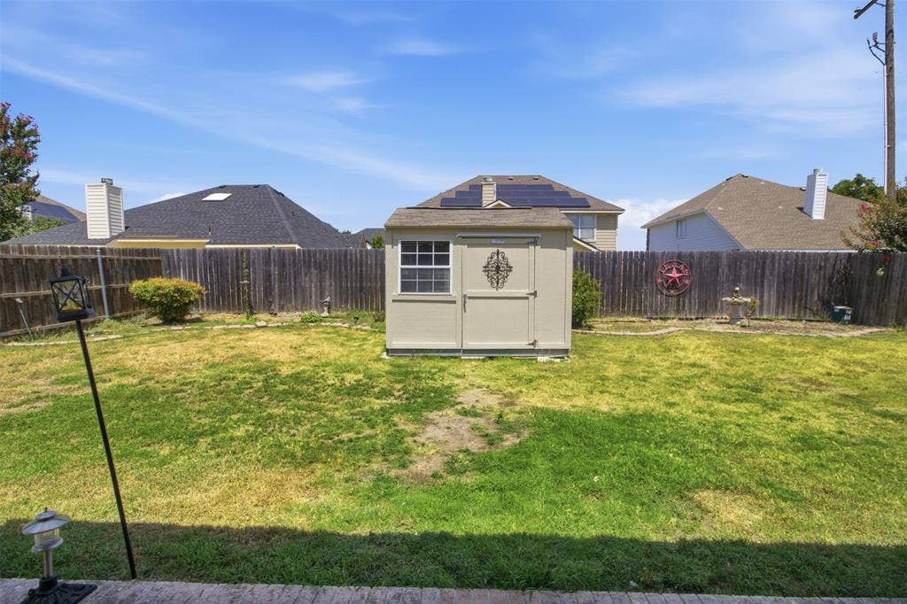 1112 Badbury Lane, Grand Prairie, TX 75052 Backyard featuring a wooden privacy fence, a detached storage shed, and a concrete patio edge