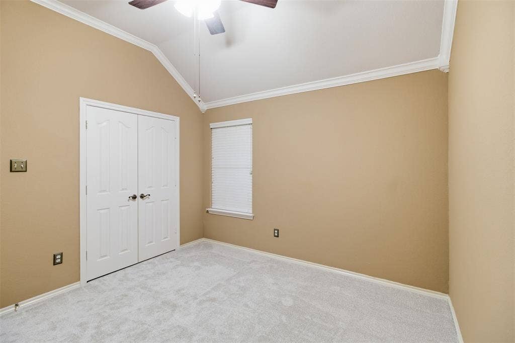 1112 Badbury Lane, Grand Prairie, TX 75052 Vaulted ceiling with crown molding, double bifold doors, window with horizontal blinds, ceiling fan with light, and light-colored carpeting