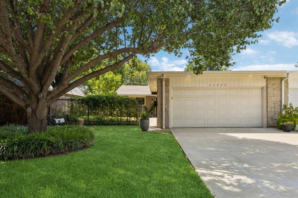 Attached garage with a panel door, stone accents, and an expansive driveway
