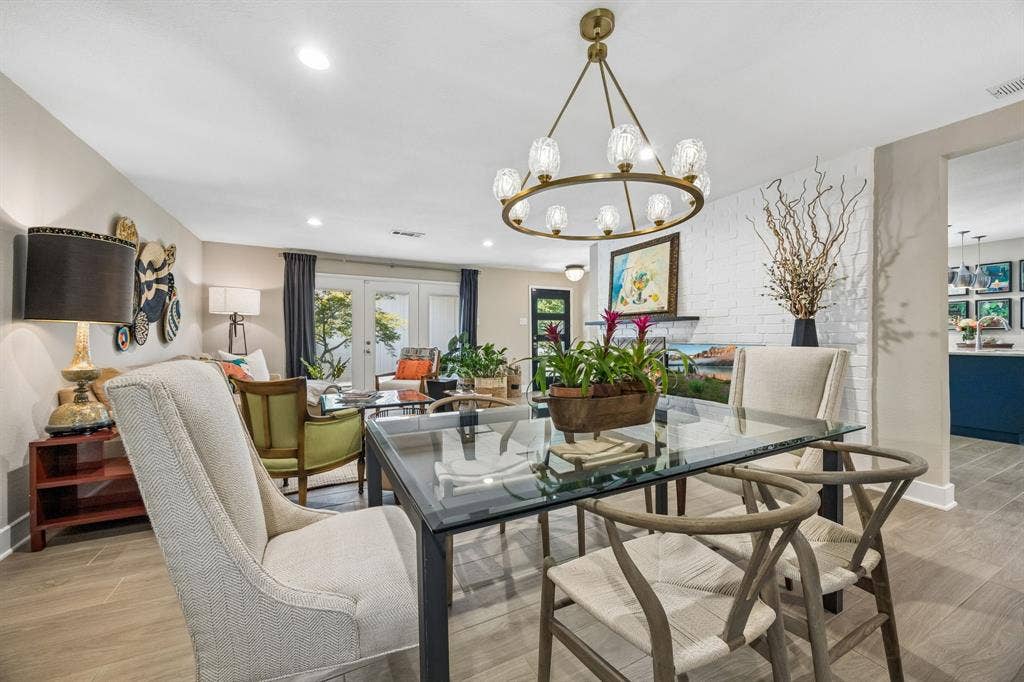 Open-concept living space tile flooring, a contemporary chandelier, white brick accent wall, and double French doors