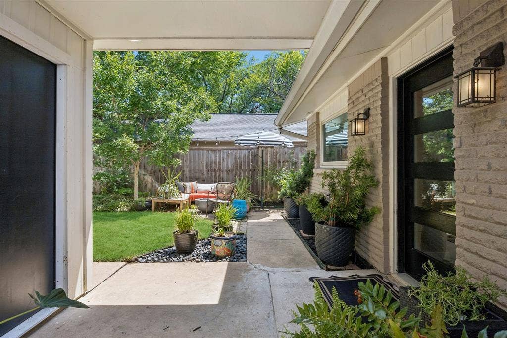 Expansive outdoor patio with concrete walkway, brick exterior, modern black-framed door, and exterior lighting fixtures