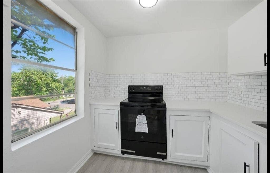 White subway tile backsplash, white countertops, built-in white cabinetry, black range, and wood-finish flooring