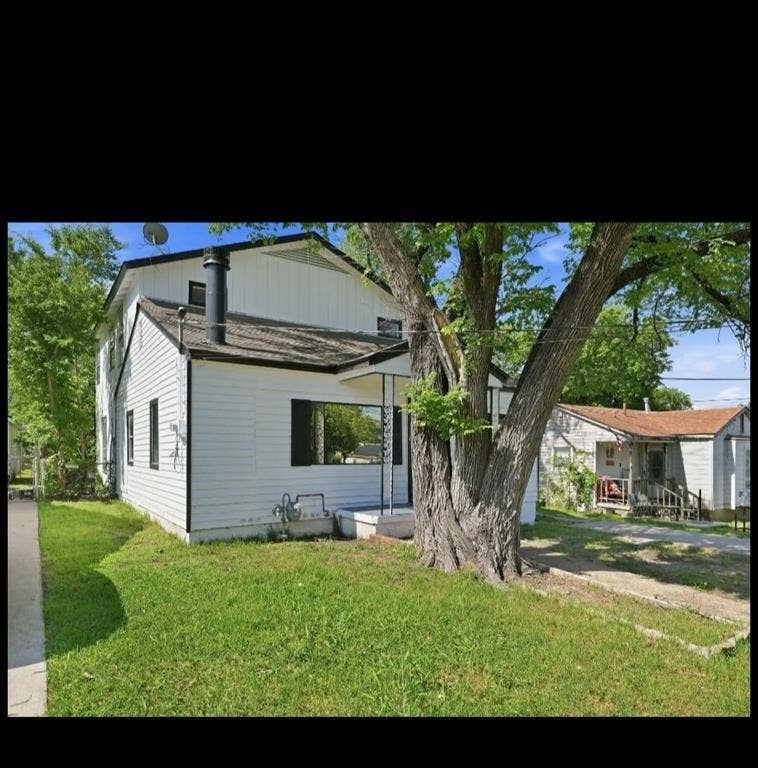 White exterior siding, dark roof, prominent chimney, mature tree, concrete pathway