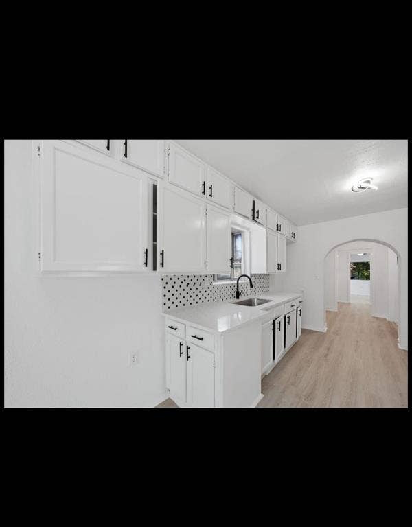 Galley kitchen featuring crisp white cabinetry with hardware accents, a polished white subway tile backsplash, stainless steel sink with modern faucet, and wood-finish flooring throughout
