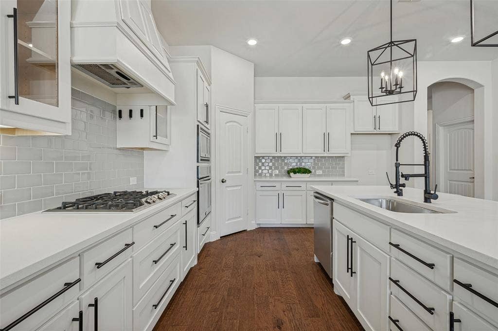 White shaker cabinetry with black hardware, stone countertops, stainless steel appliances, a gas cooktop, and wood-finish flooring