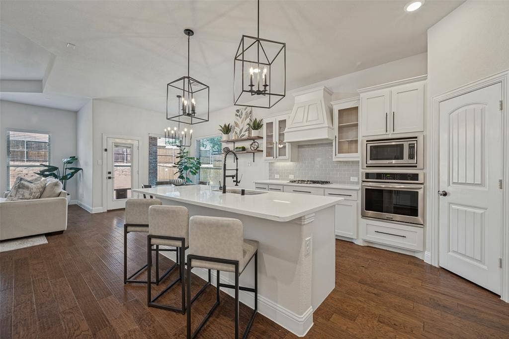 Spacious kitchen featuring an island with built-in seating, white cabinetry, integrated stainless steel appliances, and wood-finish flooring