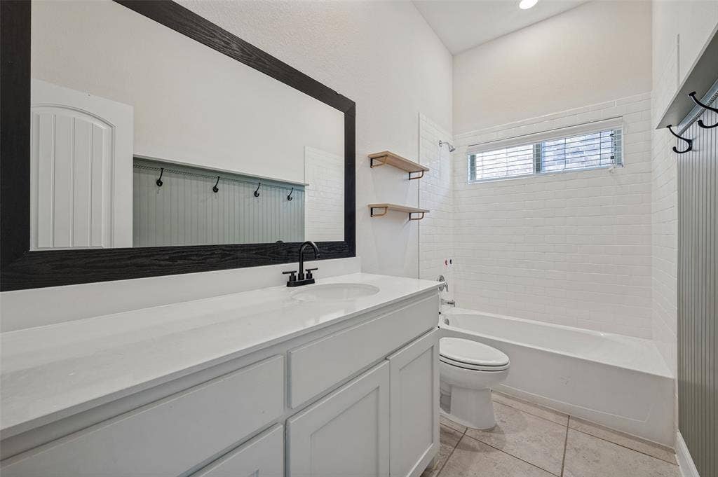 White subway tile bathtub surround, a window with blinds, a vanity with a white countertop, and a black-framed mirror