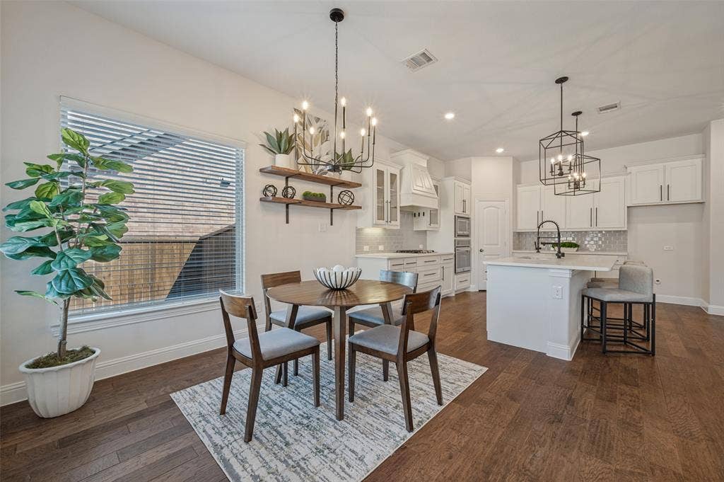 Open-concept kitchen and dining area featuring wood-finish flooring, white cabinetry, a kitchen island with seating, and a decorative tile backsplash