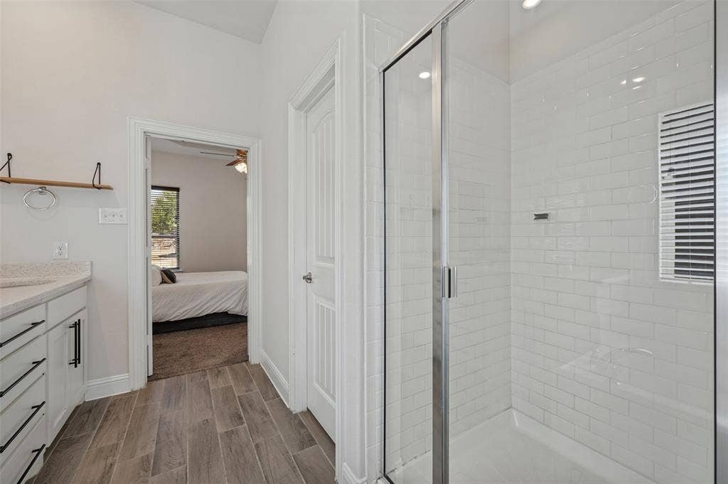 Spacious bathroom featuring wood-look tile flooring, a shower with subway tile surround, and a vanity with a light-toned countertop