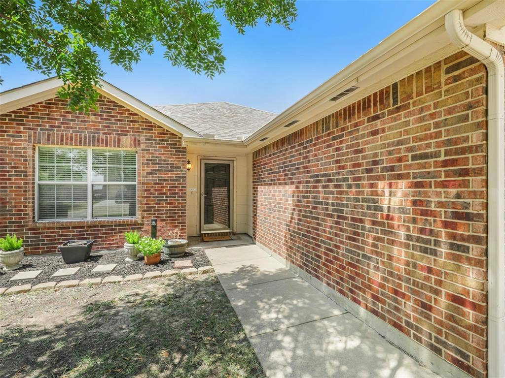 117 Palomino Lane, Krum, TX 76249 Brick home with gutters and a landscaped entry.