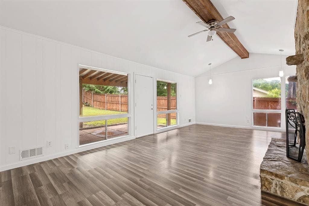 4315 Woodstock Drive, Dallas, TX 75232 Spacious living area featuring vaulted ceilings, exposed wood beam, a stone-clad fireplace, wood-finish flooring, and multiple windows