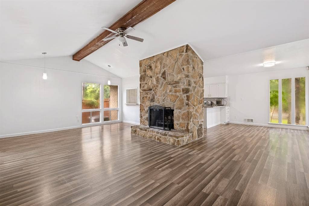4315 Woodstock Drive, Dallas, TX 75232 Vaulted ceiling with exposed wood beam, wood-finish flooring, stone-clad fireplace with hearth, built-in kitchen cabinetry