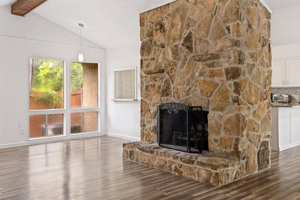 4315 Woodstock Drive, Dallas, TX 75232 Vaulted ceiling with an exposed beam, stone-clad fireplace with hearth, wood-finish flooring, and large multi-pane windows