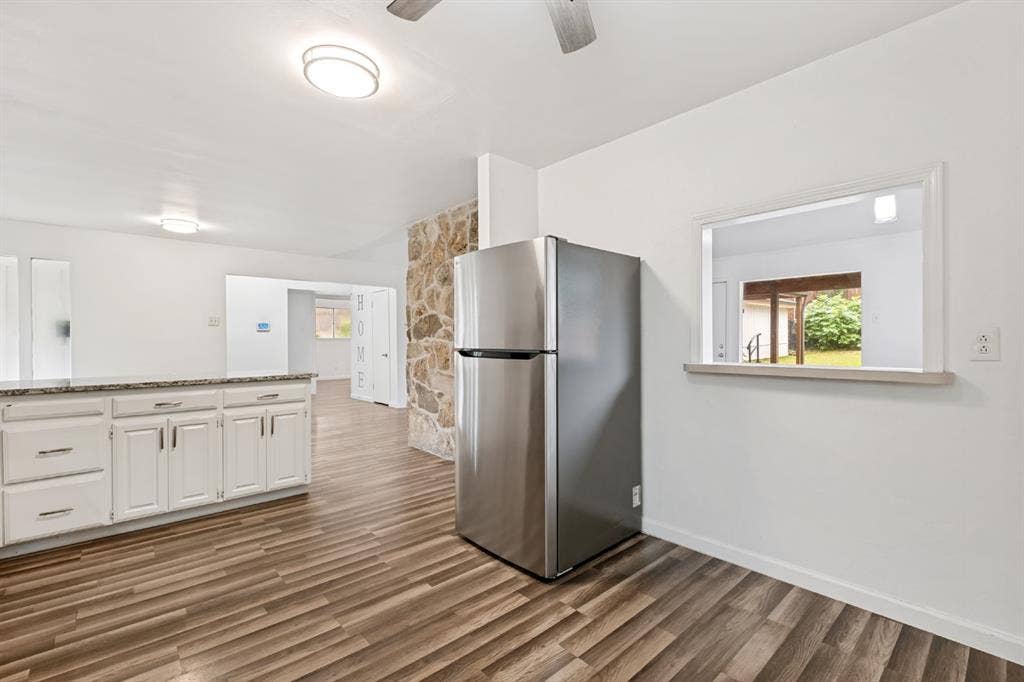 4315 Woodstock Drive, Dallas, TX 75232 Spacious kitchen featuring white cabinetry with brushed nickel hardware, stainless steel refrigerator, wood-finish flooring, recessed and ceiling-mounted lighting, and a large window providing natural light