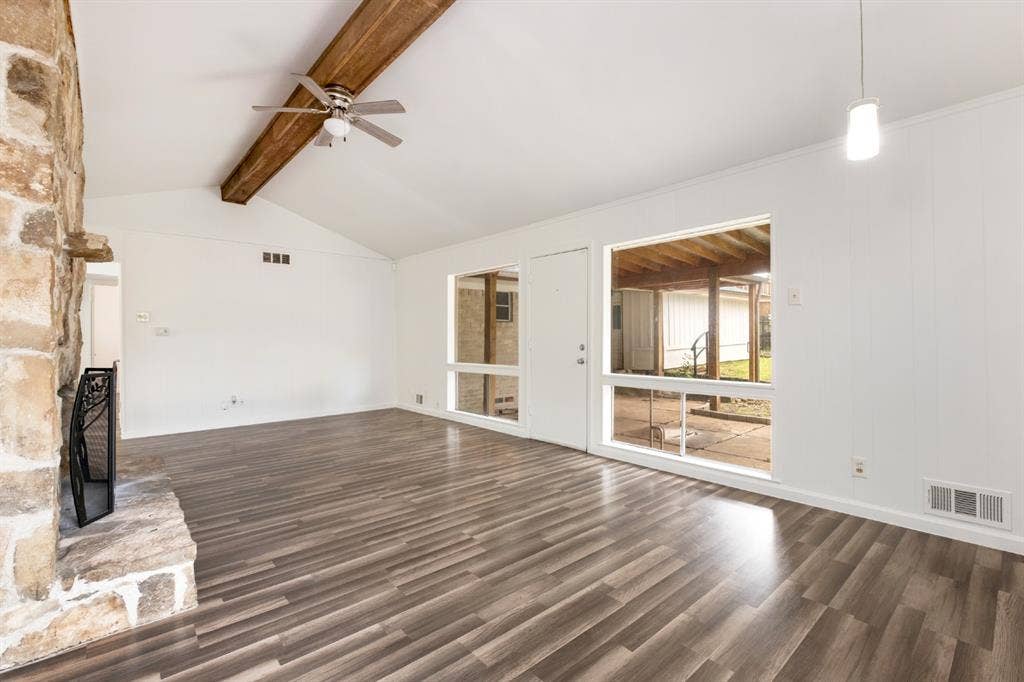 4315 Woodstock Drive, Dallas, TX 75232 Vaulted ceiling with exposed wood beam, ceiling fan, wood-finish flooring, stone-clad fireplace, and large window
