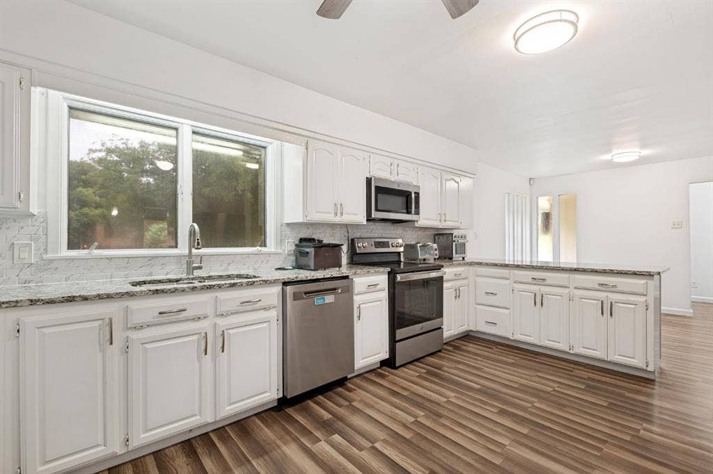 4315 Woodstock Drive, Dallas, TX 75232 Kitchen featuring white cabinetry, stainless steel appliances, speckled stone countertops, and wood-finish flooring
