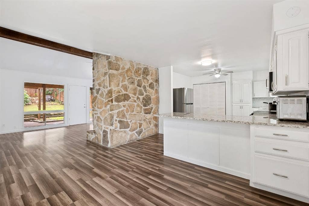 4315 Woodstock Drive, Dallas, TX 75232 Wood-finish flooring throughout, a stone-accented wall, and white cabinetry with stainless hardware