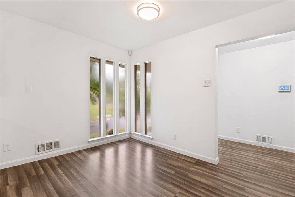 4315 Woodstock Drive, Dallas, TX 75232 Bright corner room featuring expansive multi-pane windows with natural light, wood-finish flooring throughout, and clean white walls with minimal electrical outlets and light switches visible
