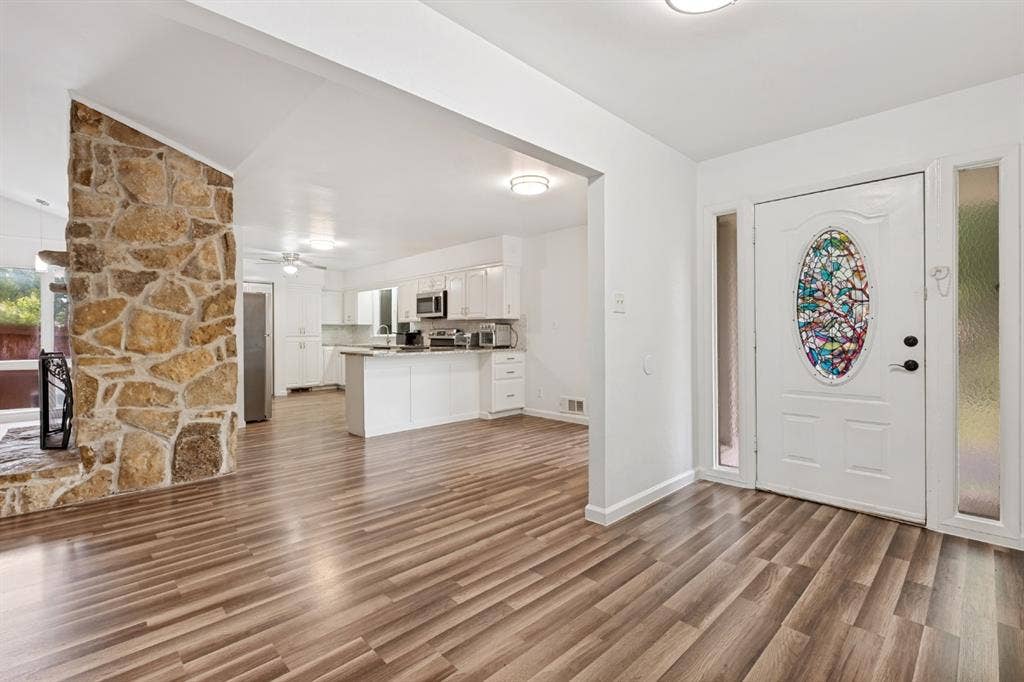 4315 Woodstock Drive, Dallas, TX 75232 Bright open-concept living area featuring warm wood-finish flooring, stone accent wall, and seamless entry to the kitchen