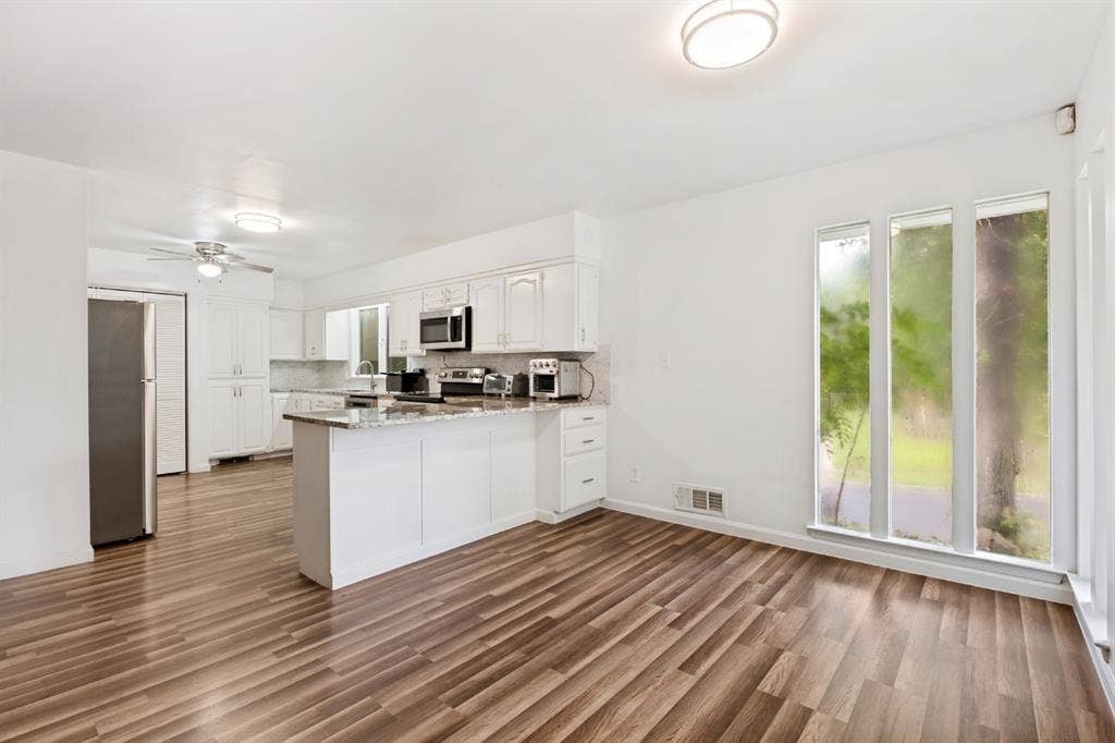 4315 Woodstock Drive, Dallas, TX 75232 White cabinetry with stainless steel appliances, wood-finish flooring, a kitchen island with a stone countertop, and large vertical windows