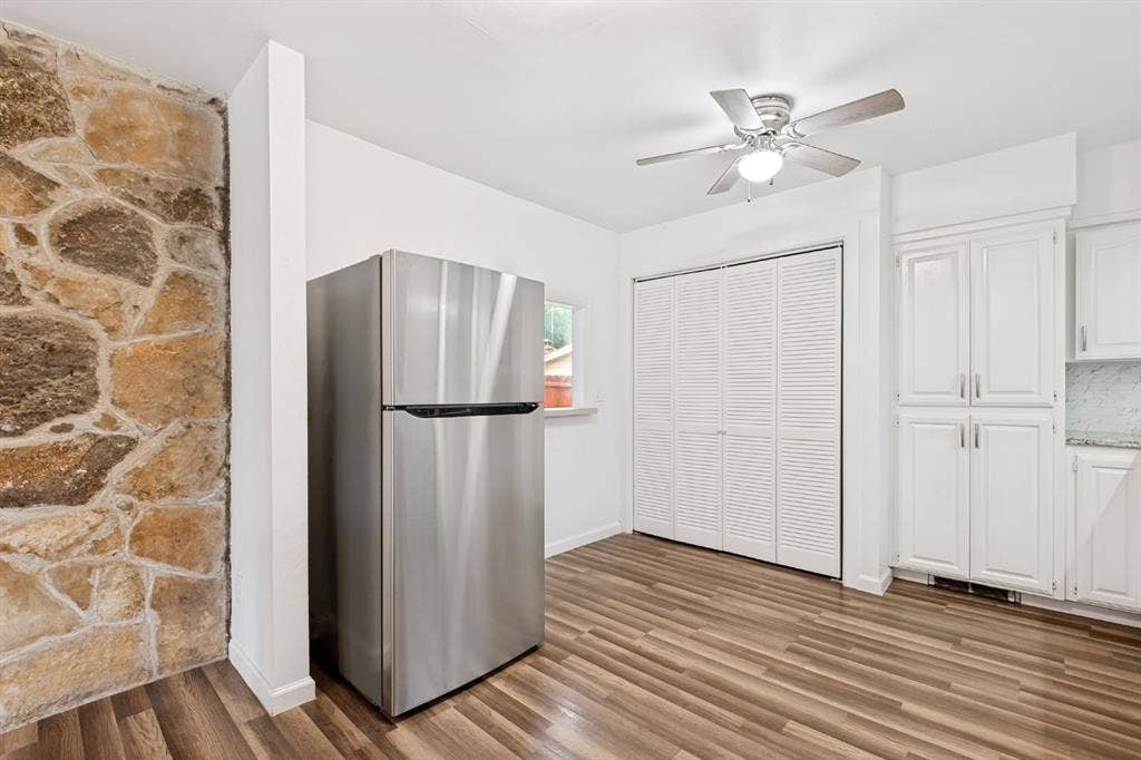4315 Woodstock Drive, Dallas, TX 75232 Stone accent wall, wood-finish flooring, stainless steel refrigerator, white shaker-style cabinetry, and ceiling fan with integrated lighting
