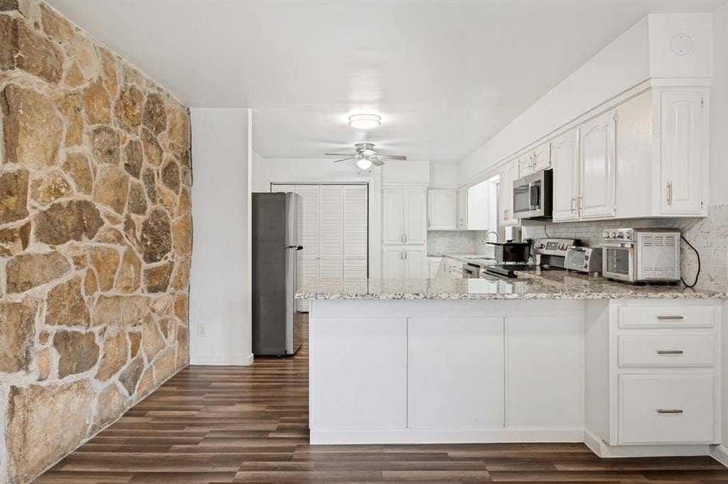 4315 Woodstock Drive, Dallas, TX 75232 Modern kitchen featuring white cabinetry with brushed metal hardware, stainless steel appliances, and a quartz countertop with subway tile backsplash