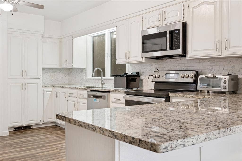 4315 Woodstock Drive, Dallas, TX 75232 Chef's kitchen featuring white cabinetry, granite countertops, stainless steel appliances including a gas range and over-the-range microwave, subway tile backsplash, and an island with extended seating