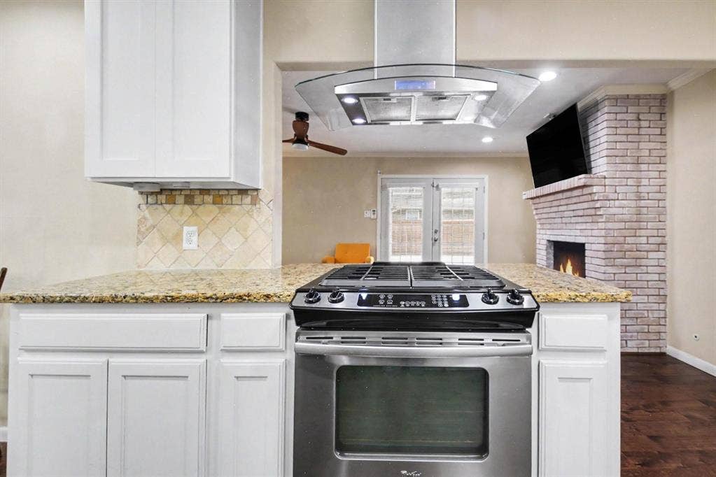 1114 Glouchester Drive, Garland, TX 75040 Stainless steel range with a coordinating range hood, granite countertops, white cabinetry, and a tile backsplash