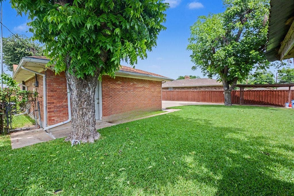 1114 Glouchester Drive, Garland, TX 75040 Expansive lawn area with mature trees, brick exterior structure, and wood privacy fencing