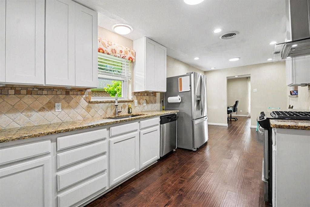 1114 Glouchester Drive, Garland, TX 75040 Well-appointed kitchen featuring white cabinetry, granite-style countertops, mosaic tile backsplash, stainless steel appliances, and wood-finish flooring