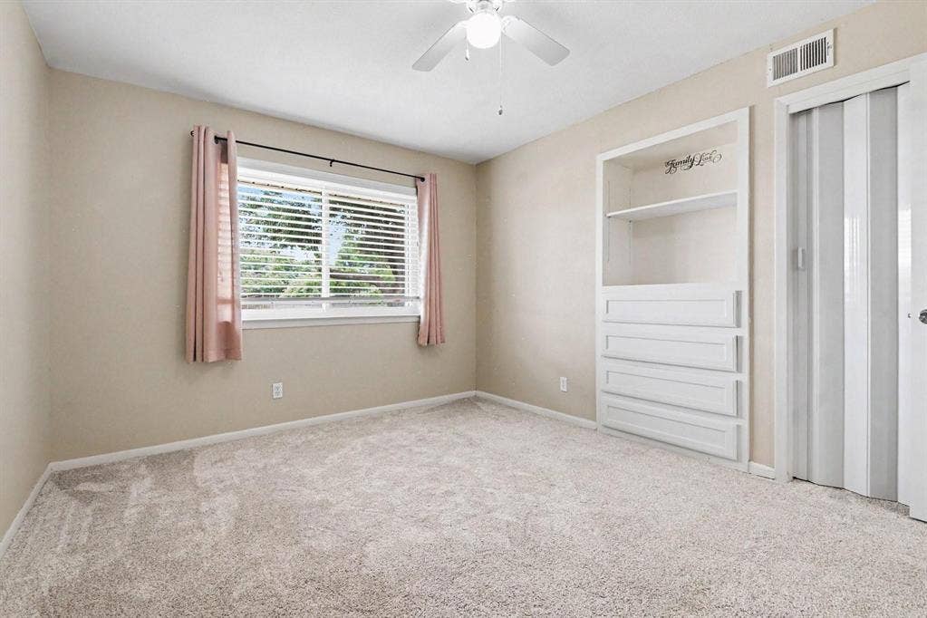 1114 Glouchester Drive, Garland, TX 75040 Light-colored carpeted flooring, built-in shelving with integrated drawers, ceiling fan with light fixture, and horizontal window blinds