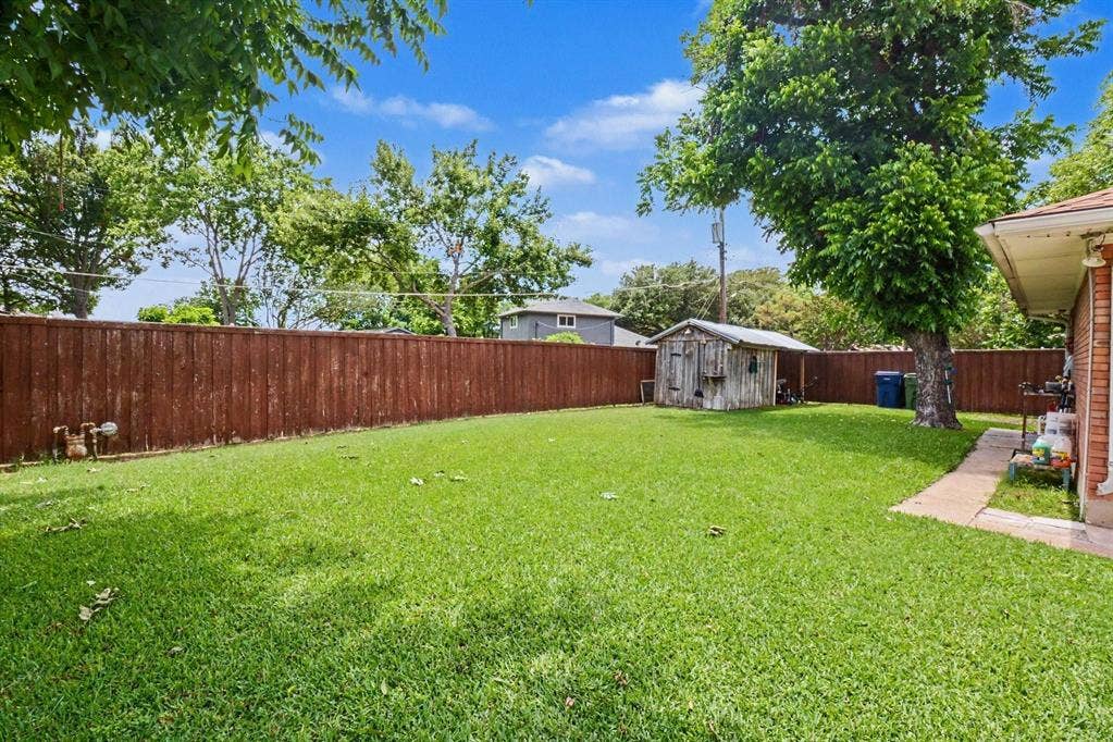 1114 Glouchester Drive, Garland, TX 75040 Spacious backyard featuring a manicured lawn, a wood privacy fence, mature trees, and a detached storage shed
