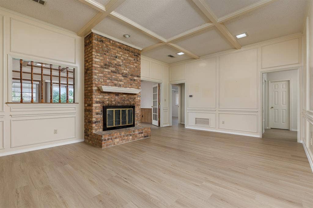 2526 Willowdale Drive, Carrollton, TX 75006 Expansive room featuring a brick fireplace, wood-finish flooring, coffered ceiling, wall paneling, and an interior window with wood detailing