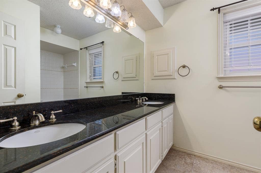 2526 Willowdale Drive, Carrollton, TX 75006 Dual vanity with dark granite-style countertop, white cabinetry, and brushed nickel fixtures
