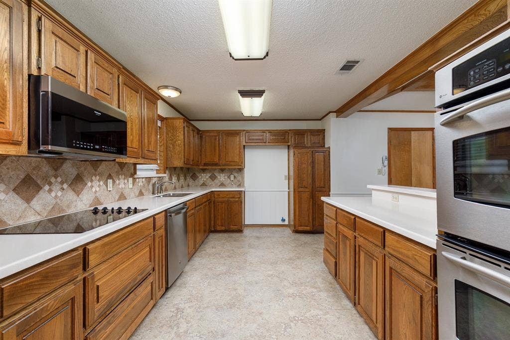 2526 Willowdale Drive, Carrollton, TX 75006 Expansive kitchen featuring wood cabinetry, white countertops, stainless steel appliances, and a tiled backsplash