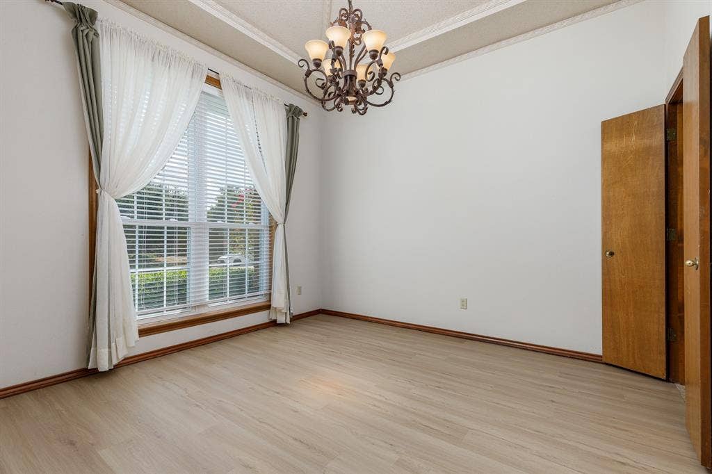 2526 Willowdale Drive, Carrollton, TX 75006 Spacious room featuring light wood-finish flooring, a large window, and an ornate chandelier